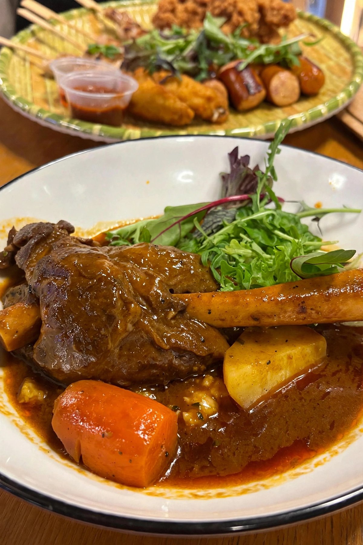 ARFC's braised lamb shank with carrot, potato and salad in a white bowl, with the Team Mates Platter behind it