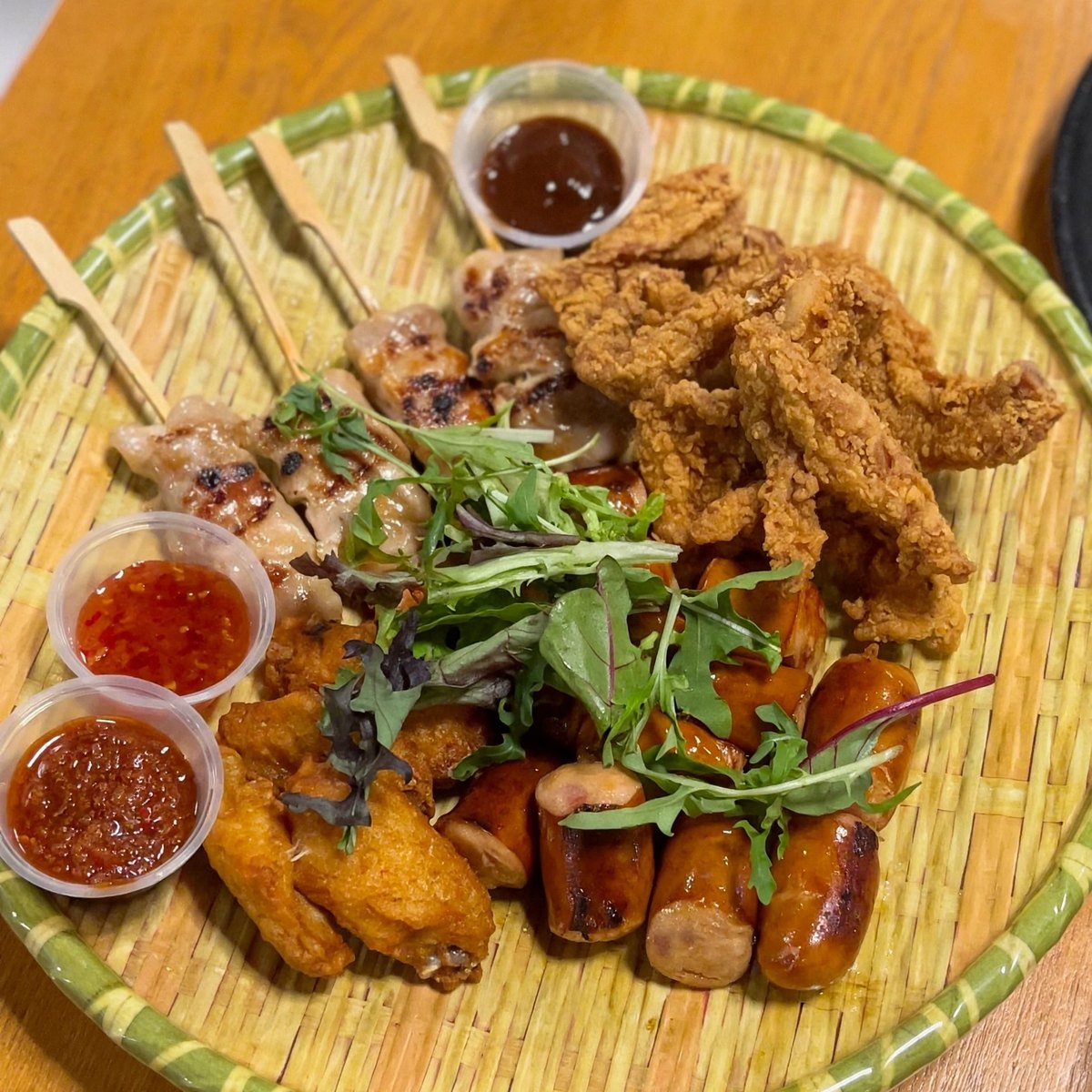 ARFC's Team Mates Platter on a woven tray, with chicken skewers, crispy chicken skin, chicken wings, chicken sausages and three dipping sauces